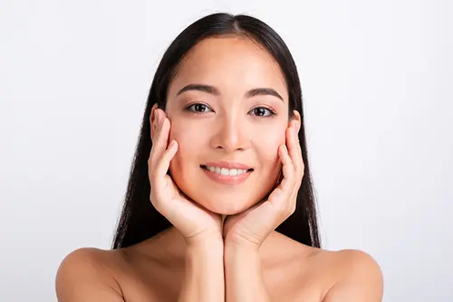 Primer plano de una mujer asiática con piel uniforme y radiante tras tratamiento facial.