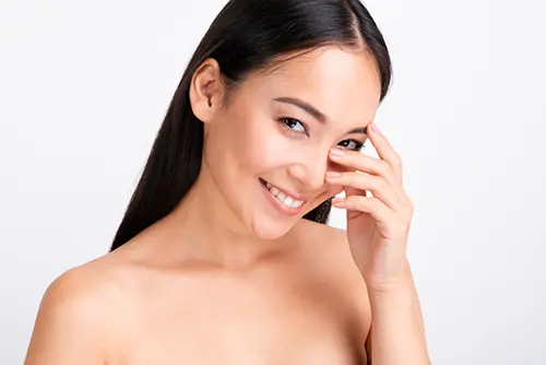Mujer asiática en primer plano sonriendo y cubriéndose parcialmente el rostro con la mano.